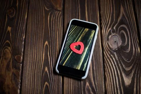 Smartphone on wooden background and a heart symbol on the screen Stock Photos