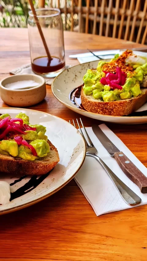 Smashed avocado toast with pickled onions on a wooden cafe table in bright Stock-Footage 328964131