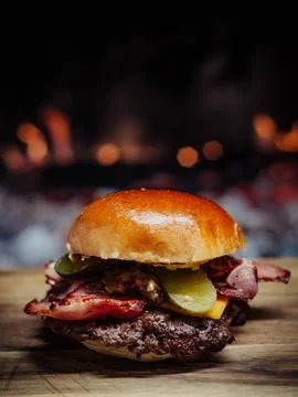 Smashed Cheeseburger on a wooden table in front of a fireplace. Stock Photos