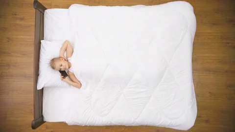 The smile boy lay on the bed and phone. Real time capture. View from above Stock Footage 71963874