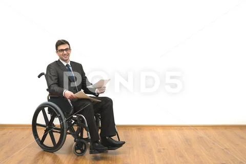 The smile disabled in a wheelchair holding papers on the white wall backgroun Stock Photos