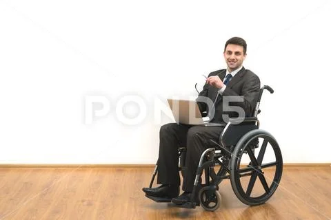 The smile man in a wheelchair sitting with a laptop on a white wall backgroun Stock Photos