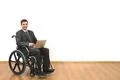 The smile man in the wheelchair works with a laptop on a white wall backgroun Photo