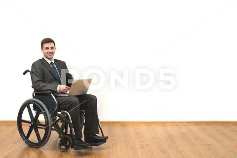 The smile man in the wheelchair works with a laptop on a white wall backgroun Stock Photos