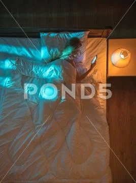 The smile woman lay on the bed and phone. Evening night time. View from above Stock Photos