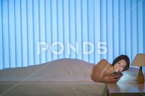 The smile woman lay on the bed and phone. Evening night time Stock Photos
