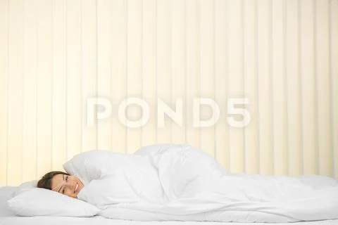 The smile woman lay on the bed on the background of a blind Stock Photos