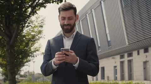 Smiled Young Bearded Man browsing his Smartphone near modern Office Building.  Video stock 113276595