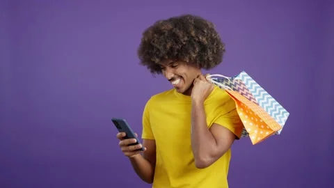 Smiley african man using the mobile while holing shopping bags Video stock 235655107