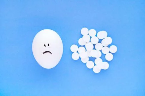 Smiley faces on eggs and white aspirin tablets next to them. Stock Photos