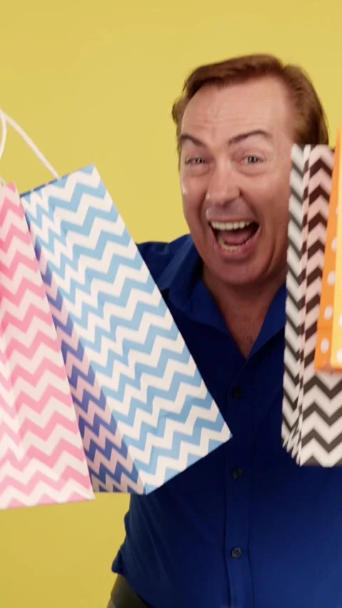 Smiley mature man looking at the camera showing shopping bags Vídeos de archivo 242329844