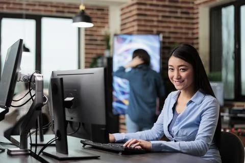 Smiling 3D artist and developer sitting at desk in office workspace while Stock Photos