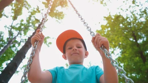 Smiling 5-year-old boy in a blue T-shirt and with a cap on his head swinging on Stock Footage 89921397