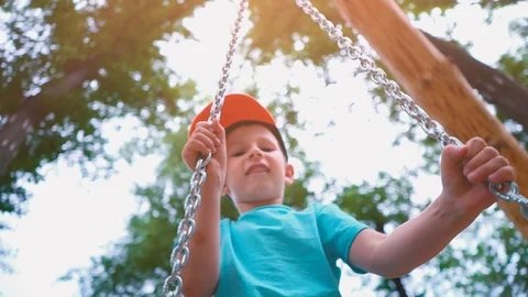 Smiling 5-year-old boy in a blue T-shirt and with a cap on his head swinging on Stock Footage 90164707