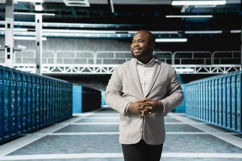 Smiling admin walking in server room, overseeing mainframes gear 스톡 사진