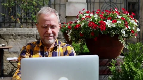Smiling adult bearded man using modern laptop outside enjoying sunny beautiful Stockbeeldmateriaal 163706989