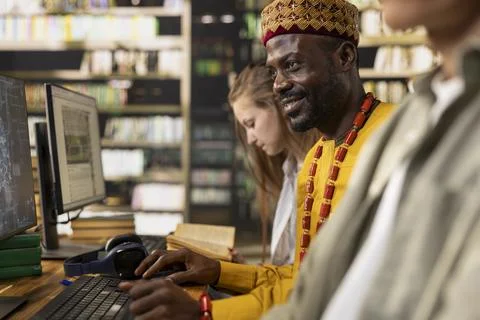 Smiling adult learner working at library table with desktop computer 写真素材