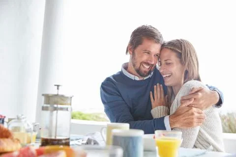 Smiling affectionate couple hugging at patio breakfast table Stock Photos