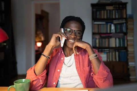 Smiling African guy college student talking on phone while studying at home Stock Photos