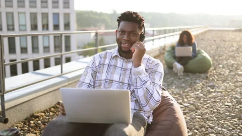 Smiling African looking at camera using portable computer and headset. Stock Footage 266069390