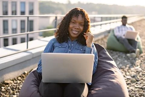 Smiling African looking at camera using portable computer and headset. 库存照片