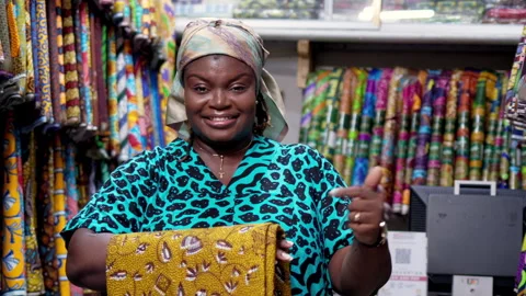 Smiling African shop owner points at Ankara fabric print textiles Video stock 346094576