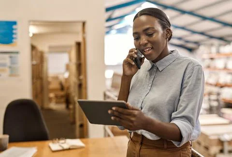 Smiling African woman using a phone and tablet in a warehouse Stock Photos