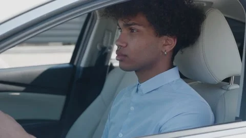 Smiling afro american guy in suit driving a car and looking at camera Stock Footage 154394493