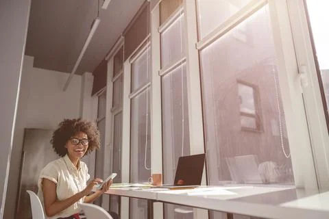 Smiling Afro American lady using phone and looking at camera Stock Photos