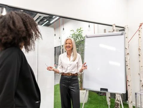 Smiling aged executive presenting project to colleague standing near whiteboa Stock Photos