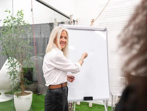 Smiling aged executive presenting project to colleague standing near whiteboa Stock Photos