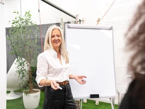 Smiling aged executive presenting project to colleague standing near whiteboa Stock Photos