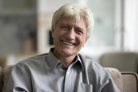 Smiling aged man sit on sofa staring at camera Stock Photos