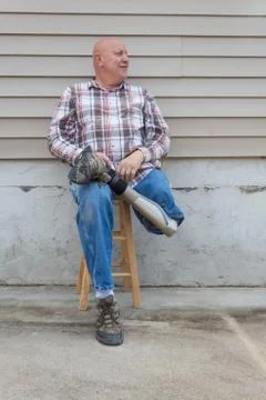 Smiling amputee man sitting on a stool, holding crossed prosthetic leg Stock Photos