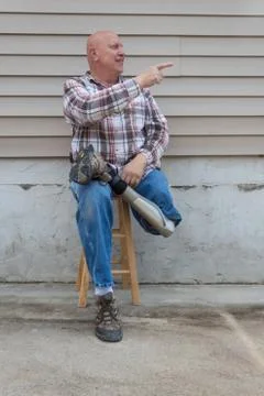 Smiling amputee man sitting on a stool, pointing Stock Photos