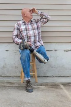 Smiling amputee man sitting on a stool, prosthetic leg crossed, shading eyes Stock Photos