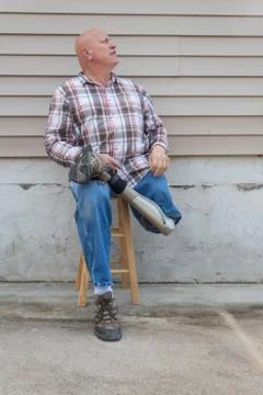 Smiling amputee man sitting on a stool, prosthetic leg crossed, looking up Stock Photos