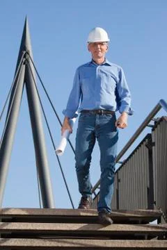 Smiling architect or engineer with hard hat and blueprint in his hand walking Stock Photos