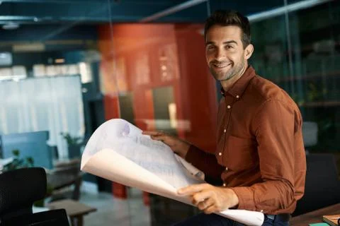 Smiling architect reading blueprints while working late in an office Stock Photos