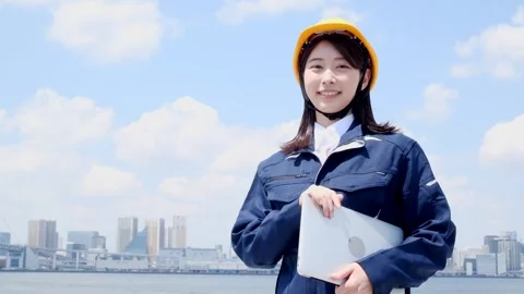 Smiling Asian Female Engineer in Hard Hat Holding Laptop Outdoors 動画素材 344091715