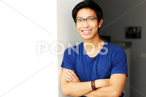Smiling asian man standing with arms folded at home Stock Photos