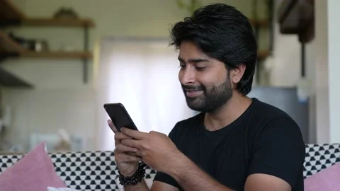 Smiling Asian Man Using Smart phone do chat while sitting at couch at home in Vídeos de archivo 154546476