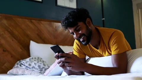 Smiling Asian Man Using Smart phone do chat while laying on bed at home indoo 動画素材 154732758