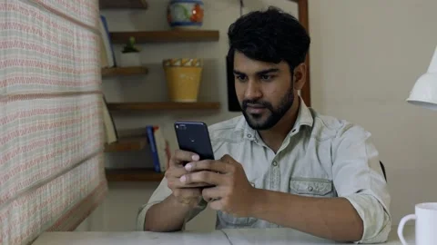 Smiling Asian Man Using Smart phone do chat while sitting on table at home in 動画素材 155575476