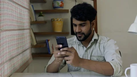 Smiling Asian Man Using Smart phone do chat while sitting on table at home in Видео 155576815