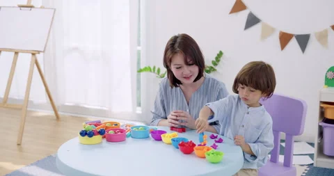 Smiling Asian mother clapping clay between palms while preschool boy shapes Stock Footage 339040065