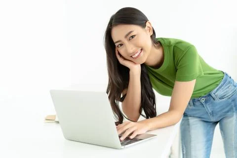 Smiling Asian standing at table with laptop and looking at camera. Stock Photos