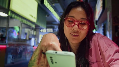 Smiling Asian Woman Using Mobile App on Smartphone in Night Cafe Stock Footage 343875867