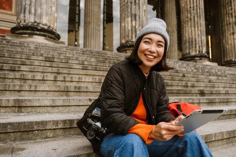Smiling asian woman using tablet computer while sitting on stairs at old ci.. Stock Photos