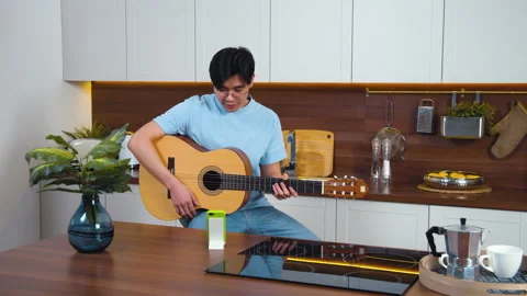 Smiling asian young man study play guitar by video call with teacher. Home kitch Stock Footage 162974978